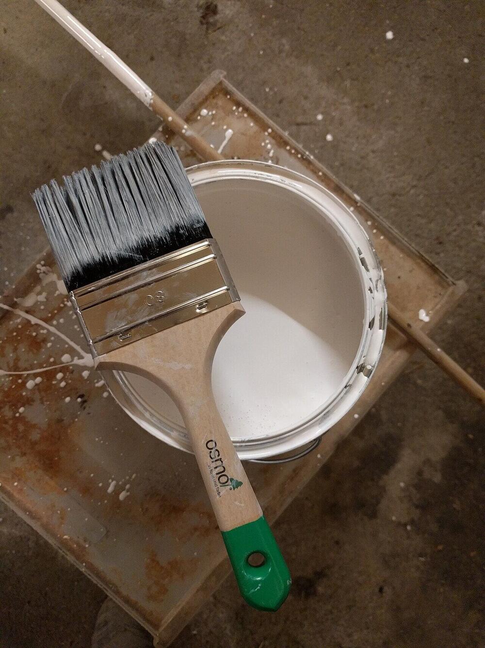 A paintbrush resting across an open can of white paint